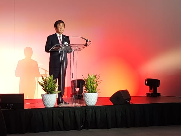 A business man in a suit stands on stage and speaks to an audience.