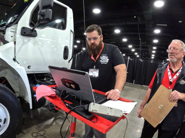 Technician working on laptop with a truck in the background.