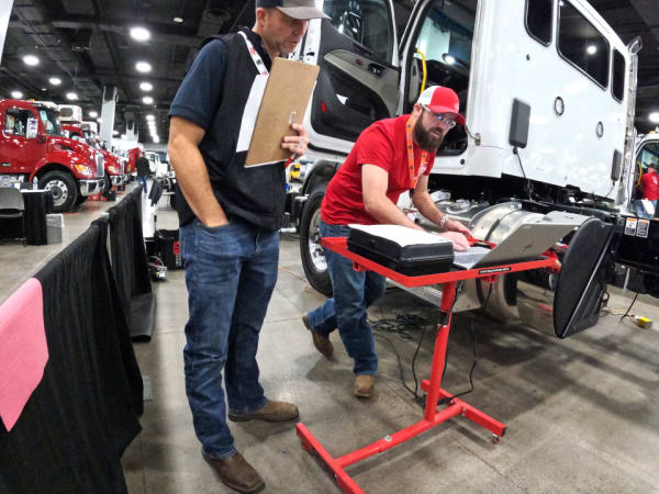 Technician working on laptop with a truck in the background.