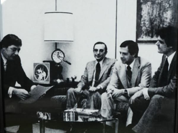 Black-and-white photo of four business professionals meeting in an office during EMKAY’s early years.