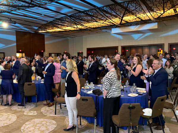 Attendees of awards dinner stand and cheer. 