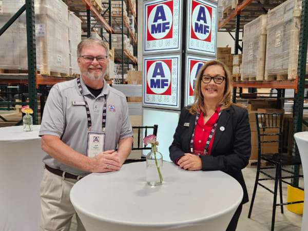 A man and a woman stand at a round table in a warehouse.