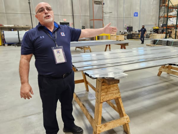 An AMF Bruns employee stands in a warehouse and gestures to metal materials on tables.