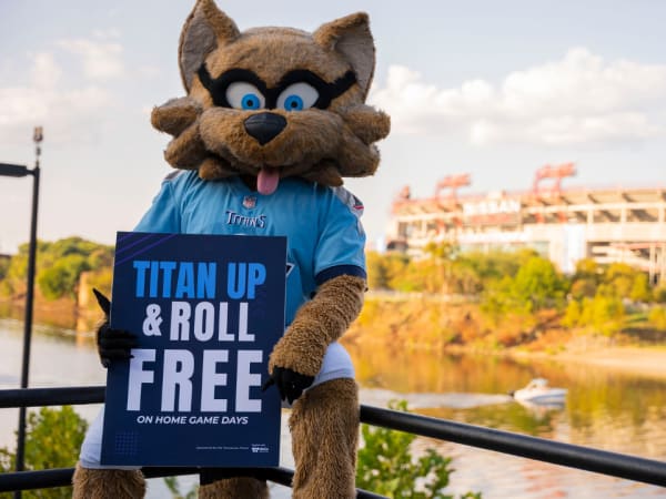 The NFL's Tennessee Titans' mascot, T-Rac, sits on a railing and holds a sign promoting free public transit rides on game day.