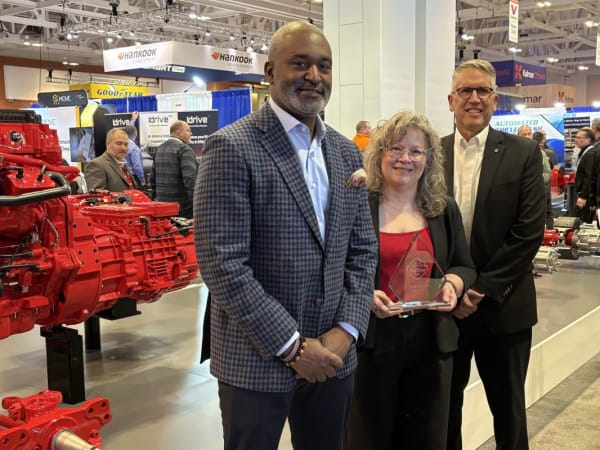 Two men and one woman posing by red engine with Top 20 trophy
