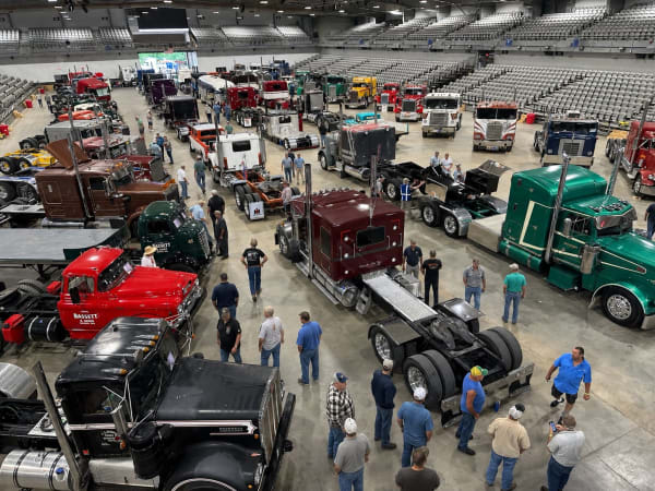 People walking among antique trucks inside a show arena