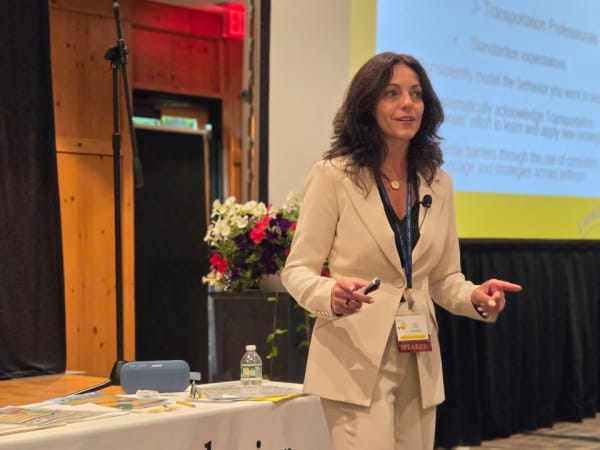 Child Behavior Consulting founder Lisa Navarra presents an educational session, speaking to attendees while standing beside a presentation screen and training materials.