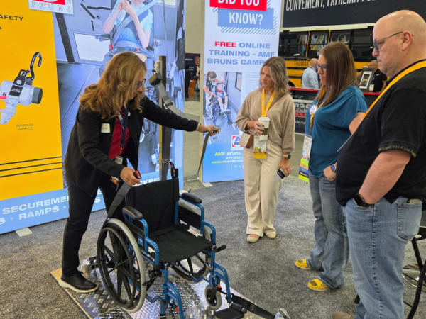 An AMF-Bruns of America representative demonstrates wheelchair securement equipment to attendees at the company's NAPT ACTS 2026 trade show booth.