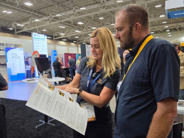 Collins Bus representative Libby Kimmel reviews a vehicle information sheet with an attendee at NAPT ACTS 2026, with school buses and other exhibitors visible behind them.