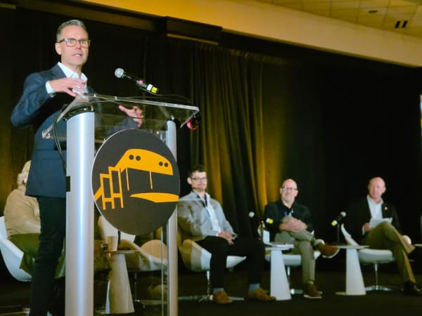 A speaker addresses the audience during a NAPT ACTS 2026 session on school bus manufacturing and industry developments, with panelists seated behind him.