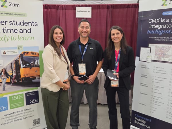 Three Zum representatives pose at their NAPT ACTS 2026 booth between displays highlighting the company's Connected Mobility Experience and CMX student transportation software.