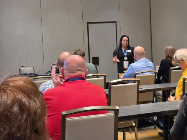 A presenter leads a small-group discussion during a NAPT ACTS 2026 regional meeting as school transportation professionals listen from tables.