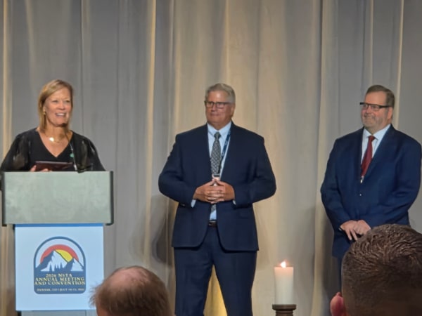 Chloe Williams of B.R. Williams speaks at the podium after receiving NSTA's 2026 Contractor of the Year Award during the Awards and Installation Dinner. NSTA leaders Patrick Dean and Curt Macysyn stand beside her on stage in Denver.