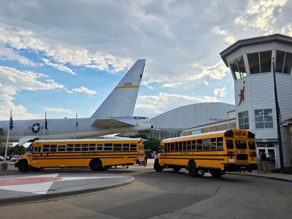 Two yellow school buses arrive outside the Wings Over the Rockies Air & Space Museum as attendees gather for an evening networking event during the 2026 NSTA conference.