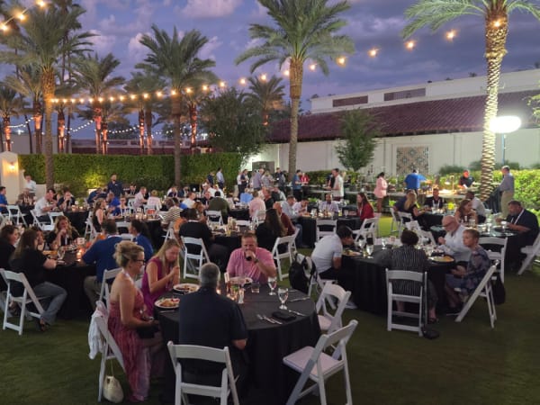 School Bus Fleet Connex attendees dine outdoors beneath string lights and palm trees during an evening networking event.
