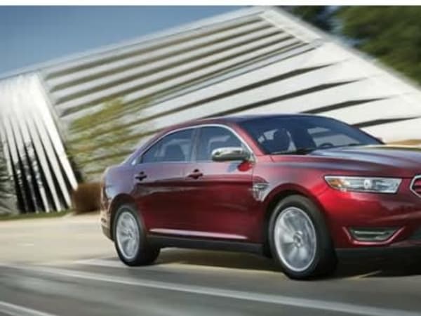 A red Ford taurus driving on the road