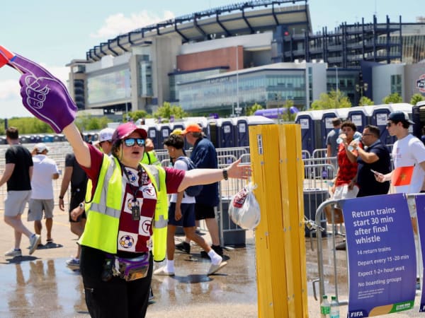 A woman with a large purple foam finger and hi-vis vest directs World Cup attendees.