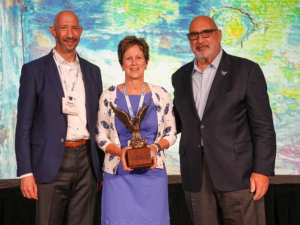 Award winner holding trophy is flanked by two men posing for camera. 