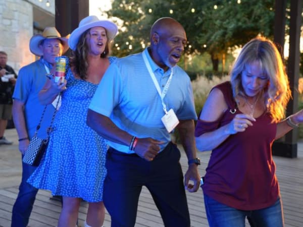 Three attendees line dancing outdoors. 