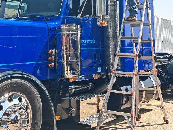 Man standing on ladder polishing exhaust stacks on a blue classic truck.