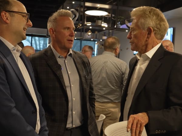 Three EMKAY professionals in suits conversing during a corporate networking event.