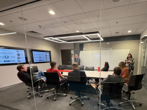 Attendees gather in a small meeting room for a presentation. 