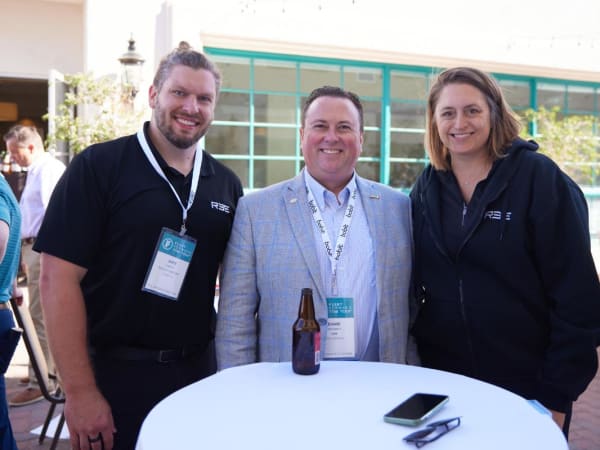Three event attendees pose at a cocktail table. 