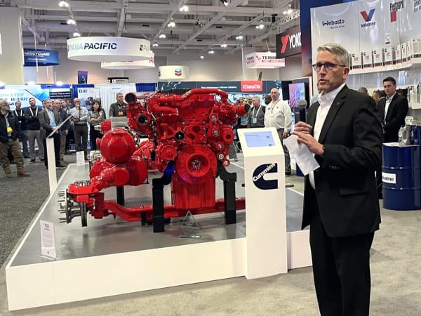 Man in suit in front of red Cummins powertrain on display