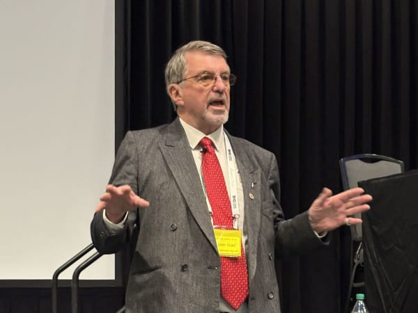 Man in sport jacket and red tie speaking to audience