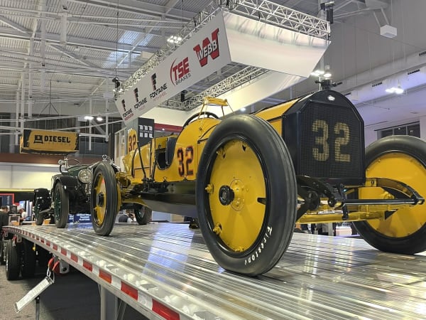 Antique yellow car on a flatbed trailer at TMC booth