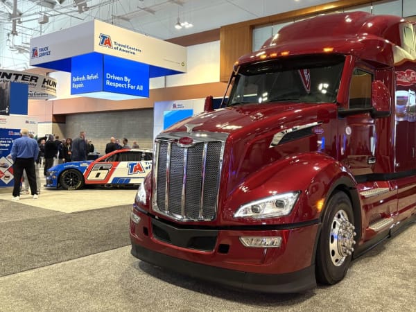 Red Peterbilt truck on TMC expo floor with racecar in the background