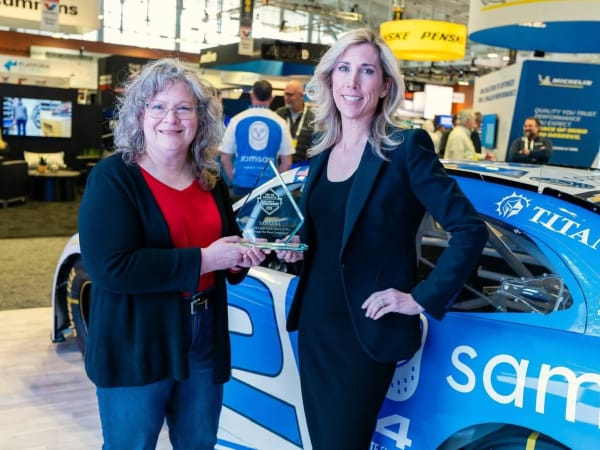 Two women shaking hands with Top 20 trophy between them in front of race car