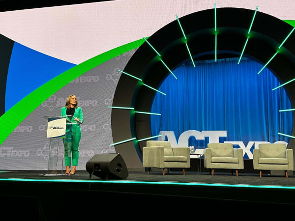 A woman on stage addresses the audience. 