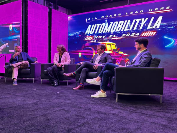 Photo of three panelists on stage during a seminar at LA Auto Show. 