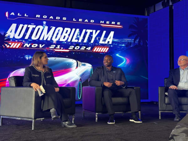 Photo of three panelists on stage at LA Auto Show. 