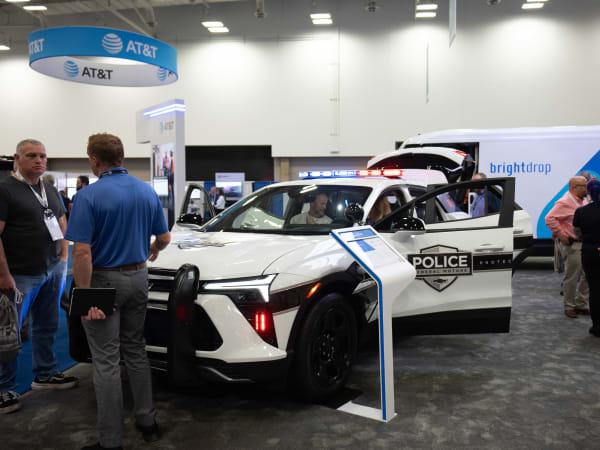 A white Chevrolet Blazer EV PPV is shown with its lights flashing and attendees gathered around it in an Exhibit Hall.