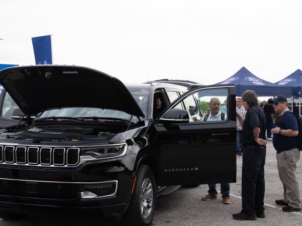 A black Jeep Wagoneer L is shown with the hood up and door open, as attendees gather around it.