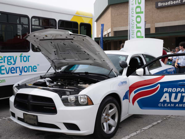 A white Dodge Charger Pursuit is shown with its hood up and door open. The vehicle has a propane autogas decal on the side.