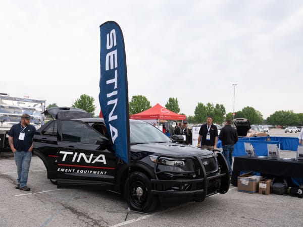 A black Ford Police Interceptor Utility with a Setina Manufacturing decal is shown with doors open and people gathered around. 