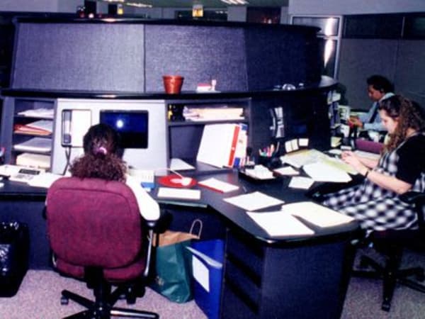 Vintage office cubicles with employees working at computers and desks in an earlier corporate workspace.
