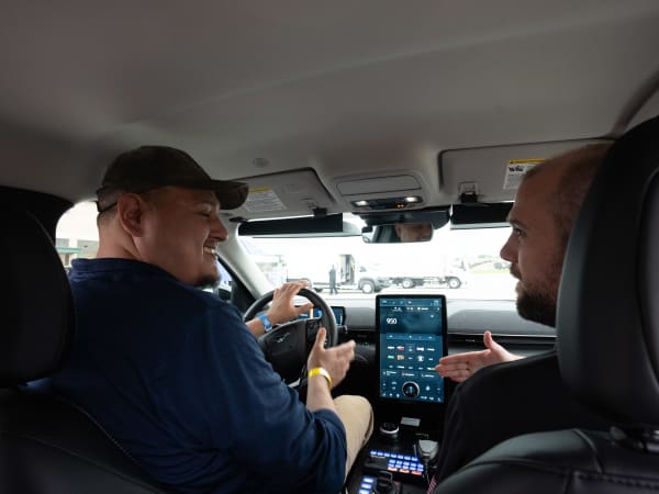 An attendee sits in the driver's seat of a Ford Mustang Mach-E, chatting with a person in the passenger's seat.
