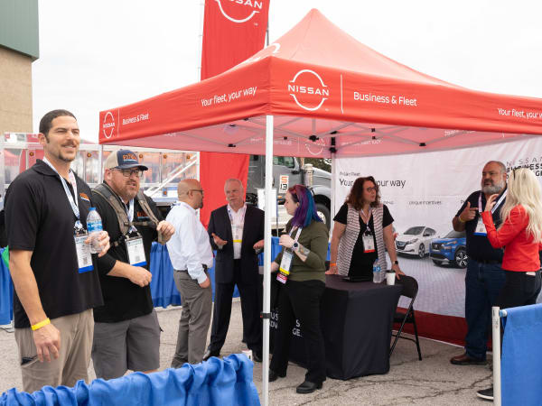 A group of people chatting under a Nissan tent is shown.