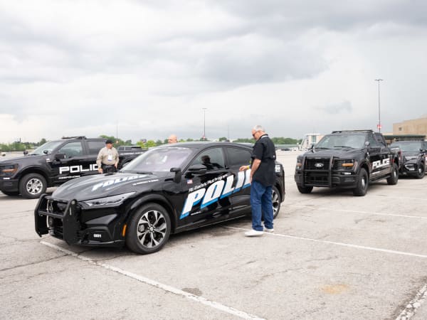 A lineup of police vehicles waiting to be test-driven is shown. They include a Ford Mustang Mach-E, a Ford F-150 Police Responder, and a Ford Police Interceptor Utility.