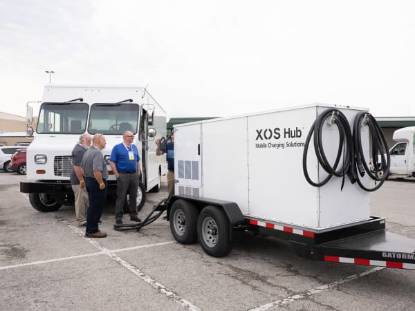 An XOS Hub mobile charging solution sits in the parking lot, with attendees looking at it.