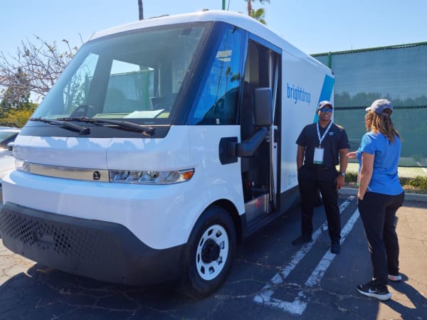 Two people talk next to an electric van. 