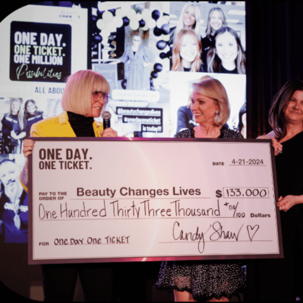 Two happy women, one wearing yellow blazer, are smiling and holding an oversized check.