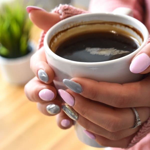 a pair of hands with pink-polished nails holding a cup of black coffee