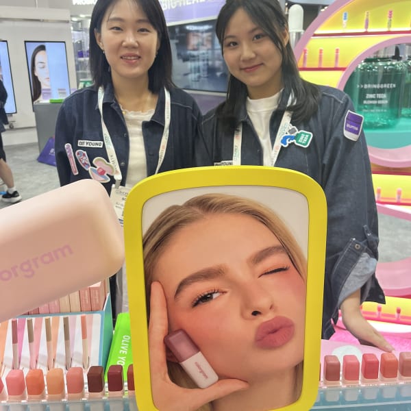 At the Olive Young booth at Cosmoprof North America, two women smile in front of a display.