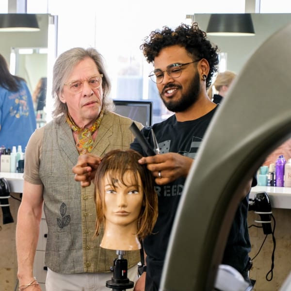 Educator Oscar Bond evaluates a student's haircut on a mannequin.