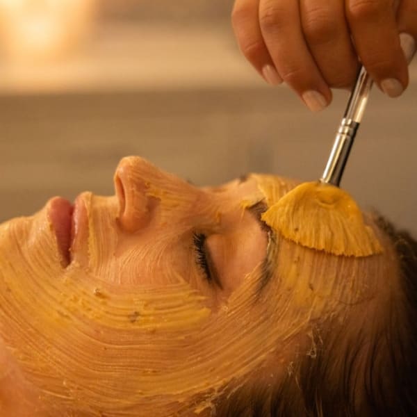 An esthetician paints a mask on a client's face during a facial